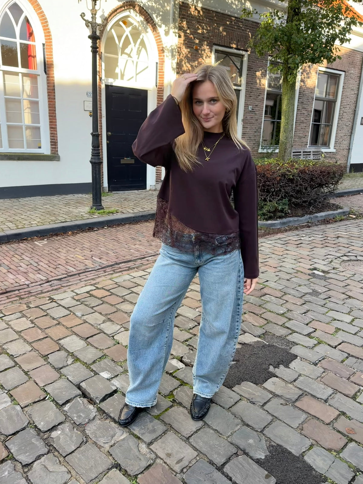 Bruine dames longsleeve met ronde hals en kanten rand aan de onderkant, gecombineerd met een lichtblauwe jeans.
