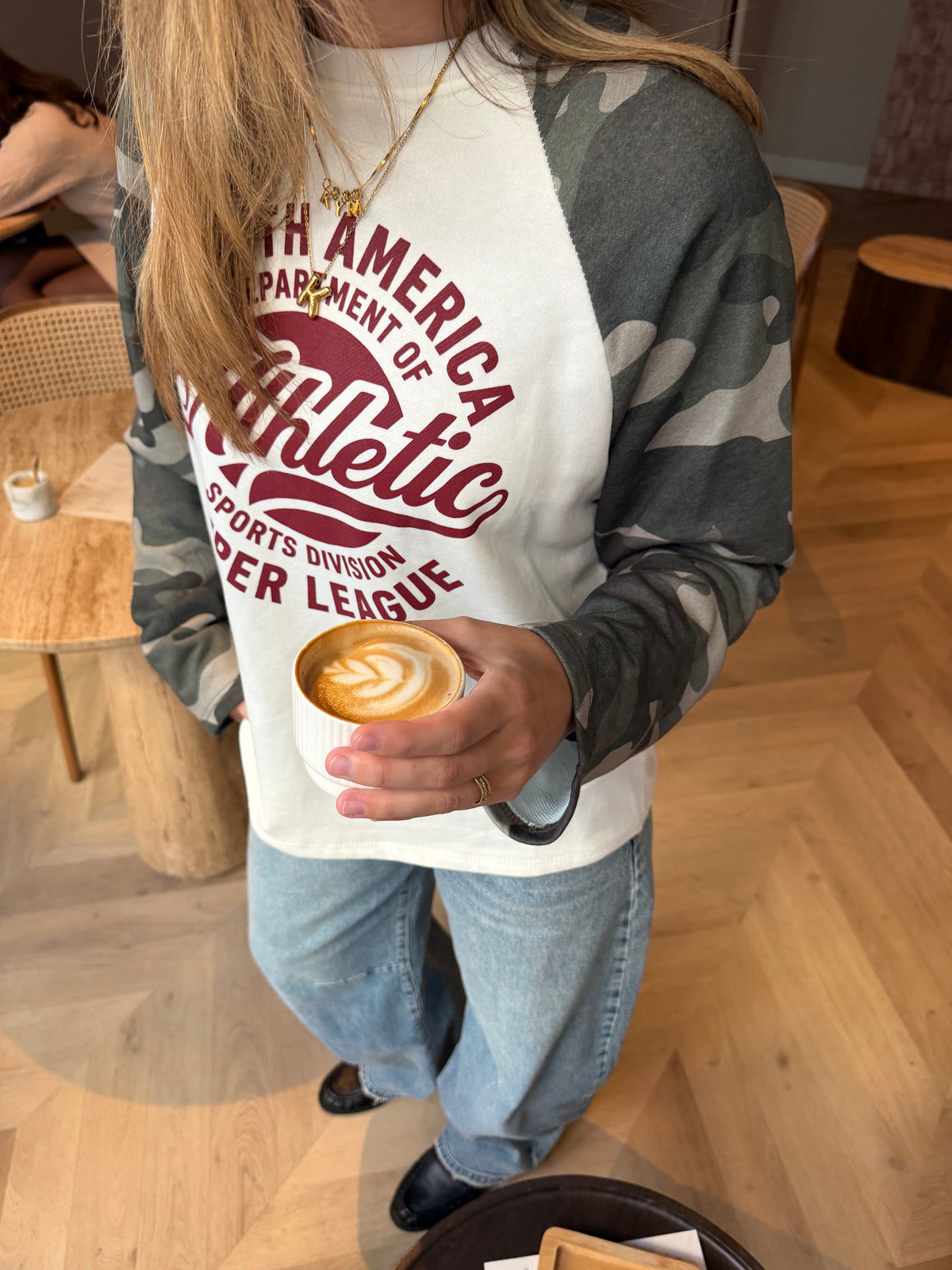Dames sweater Athletic Camo met crème voorkant, bordeauxrode tekstprint en grijze camouflage mouwen, gecombineerd met een lichte jeans