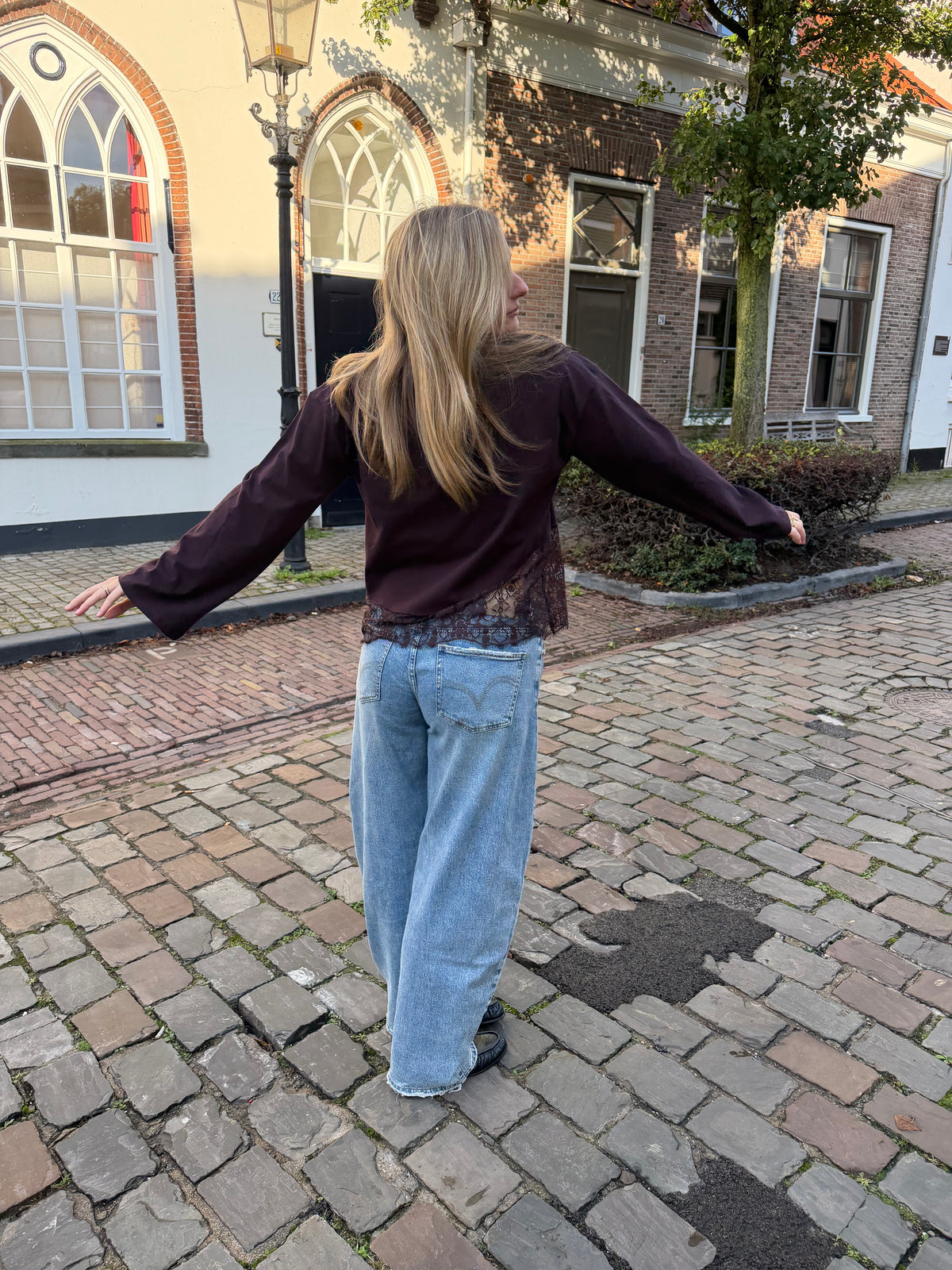 Bruine dames longsleeve met ronde hals en kanten rand aan de onderkant, gecombineerd met een lichtblauwe jeans.