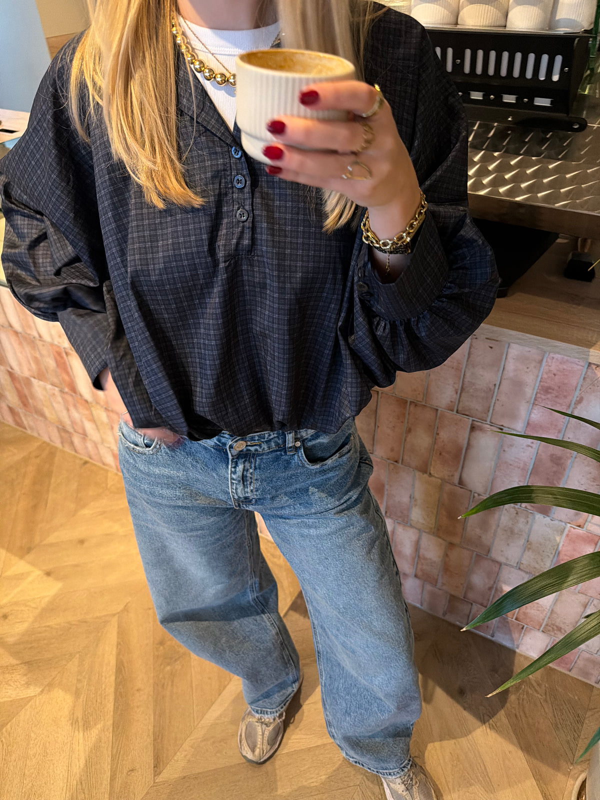 Bruine cropped damesblouse met ruitpatroon, wijde ballonmouwen en knoopsluiting, gecombineerd met een blauwe jeans.