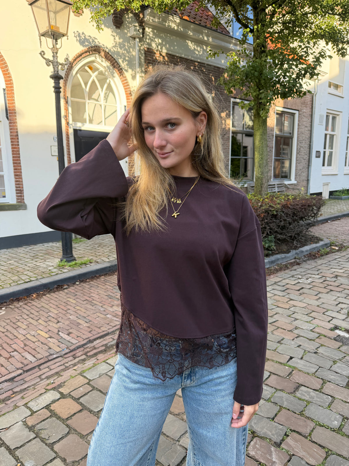 Bruine dames longsleeve met ronde hals en kanten rand aan de onderkant, gecombineerd met een lichtblauwe jeans.
