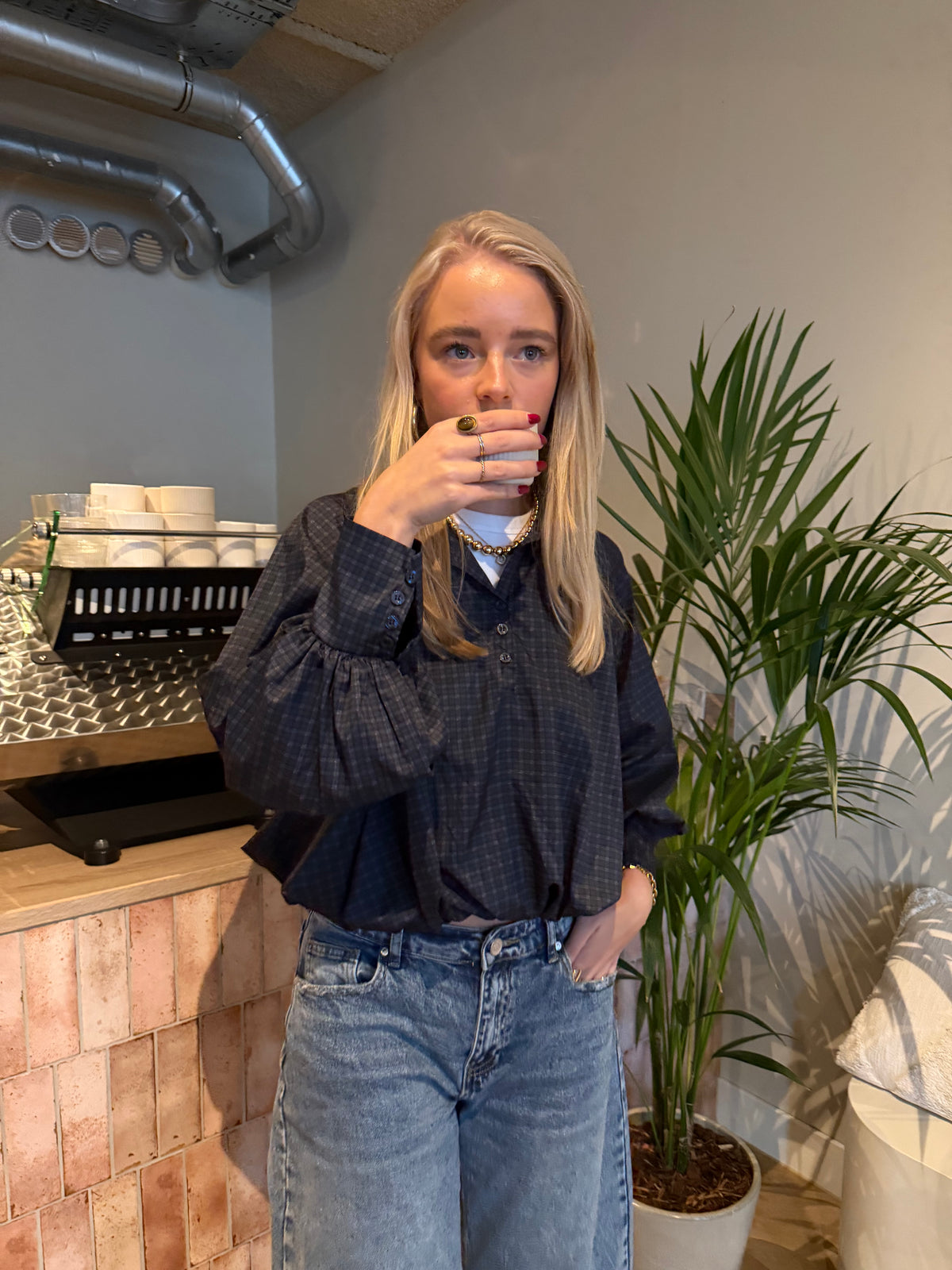 Bruine cropped damesblouse met ruitpatroon, wijde ballonmouwen en knoopsluiting, gecombineerd met een blauwe jeans.