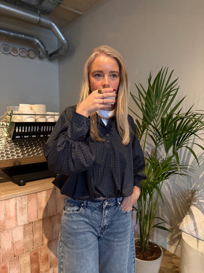 Bruine cropped damesblouse met ruitpatroon, wijde ballonmouwen en knoopsluiting, gecombineerd met een blauwe jeans.