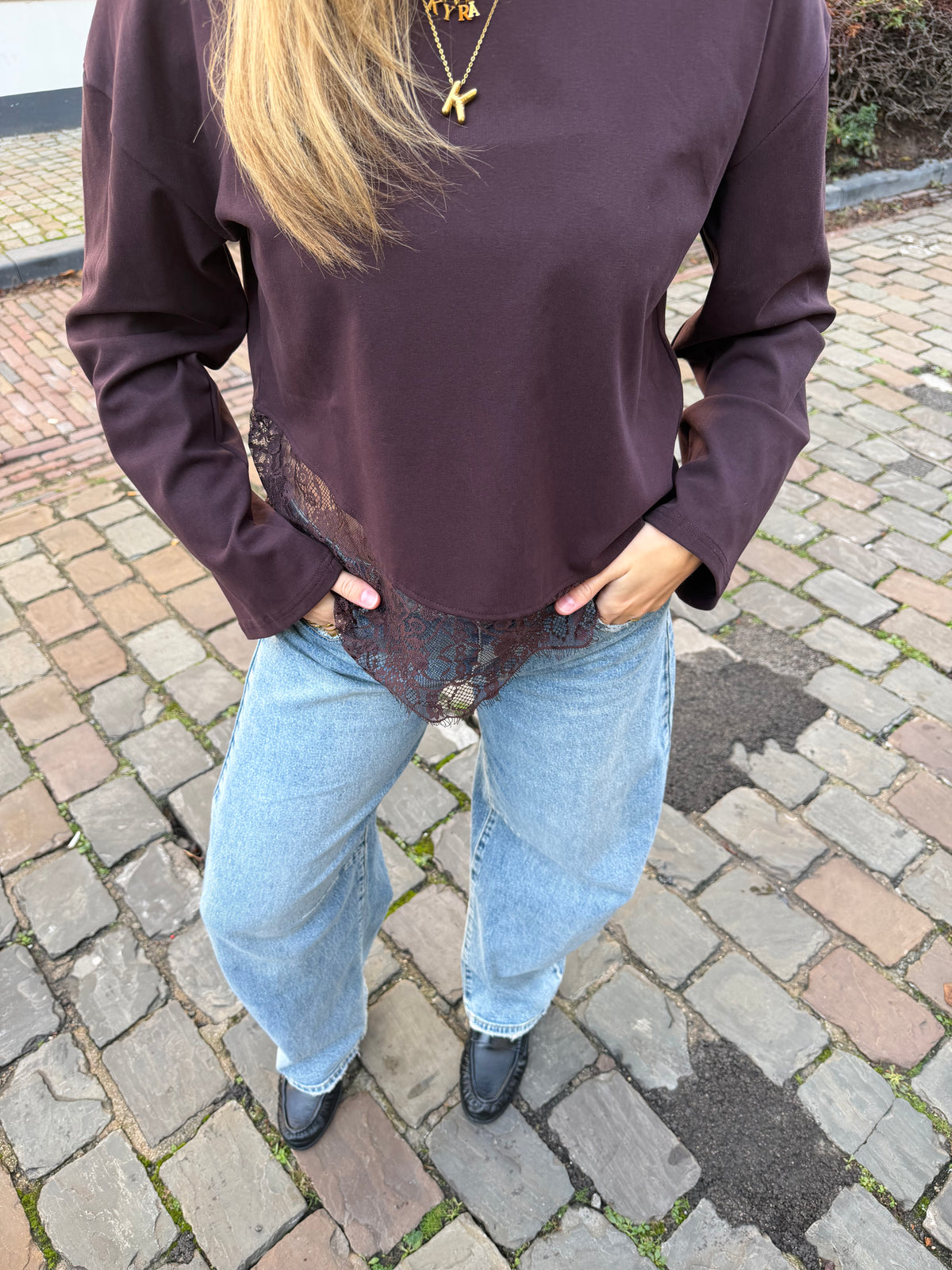 Bruine dames longsleeve met ronde hals en kanten rand aan de onderkant, gecombineerd met een lichtblauwe jeans.