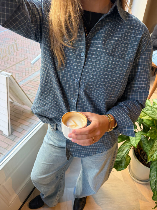 Blauwe geruite damesblouse met oversized pasvorm, kraag en knoopsluiting, gecombineerd met een lichtblauwe jeans. 