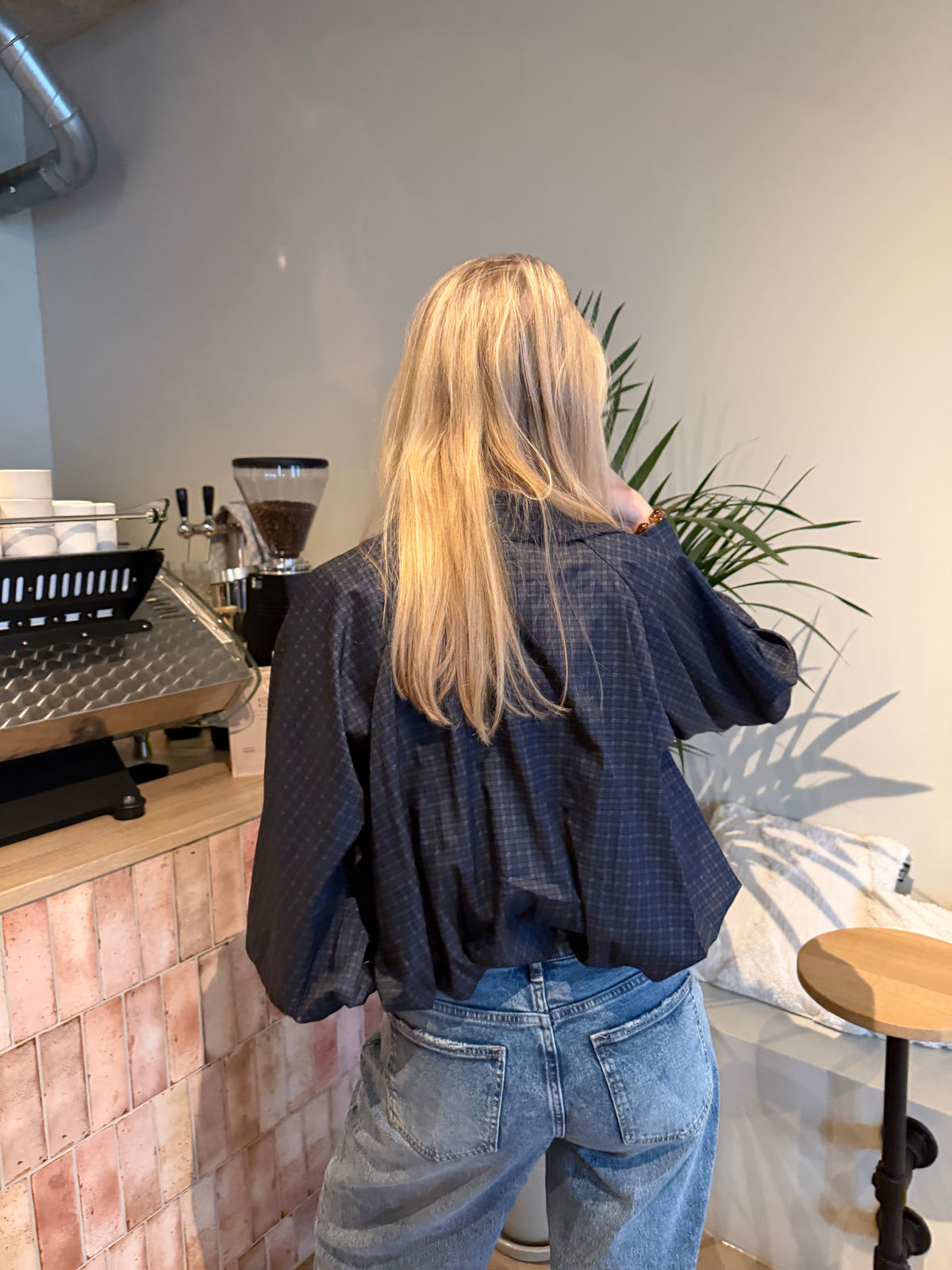 Bruine cropped damesblouse met ruitpatroon, wijde ballonmouwen en knoopsluiting, gecombineerd met een blauwe jeans.