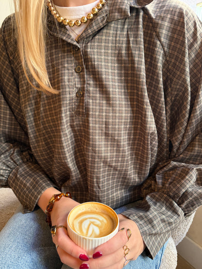 Bruine cropped damesblouse met ruitpatroon, wijde ballonmouwen en knoopsluiting, gecombineerd met een blauwe jeans.